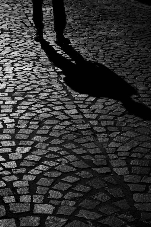 Free Shadow of a person on a cobblestone street at night creates a dramatic urban scene. Stock Photo