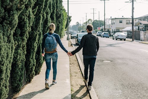 Man Holding Woman While Walking on Sidewalk