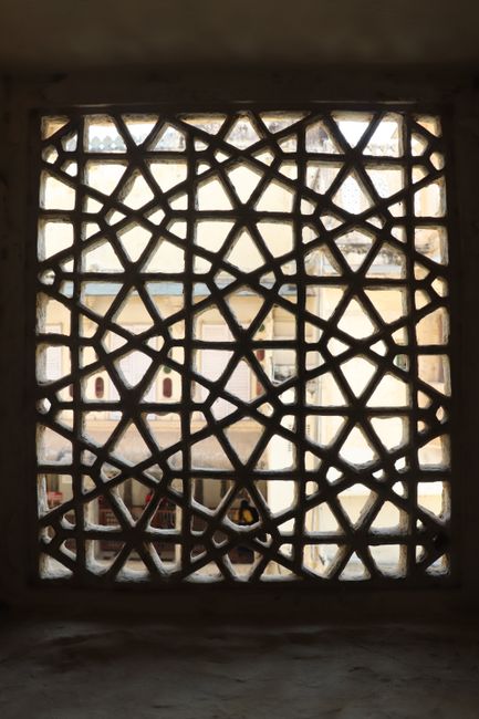 A decorative lattice window with intricate patterns frames a view of urban rooftops.