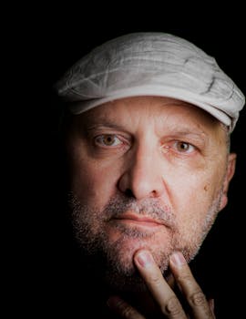 Close-up portrait of an older man with a white hat, thoughtful expression.