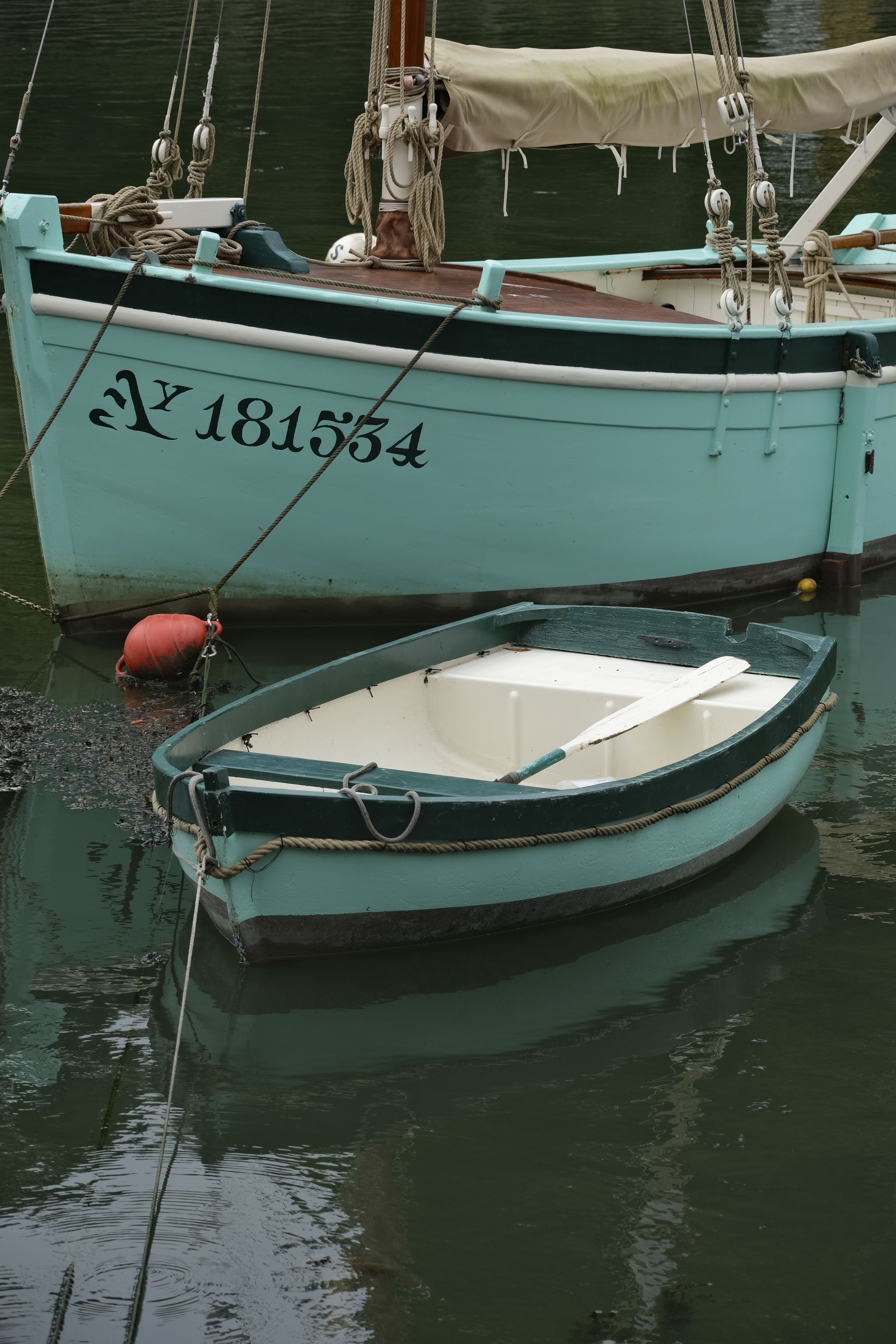 Small rowboat beside a classic sailboat in a peaceful harbor setting during the day.