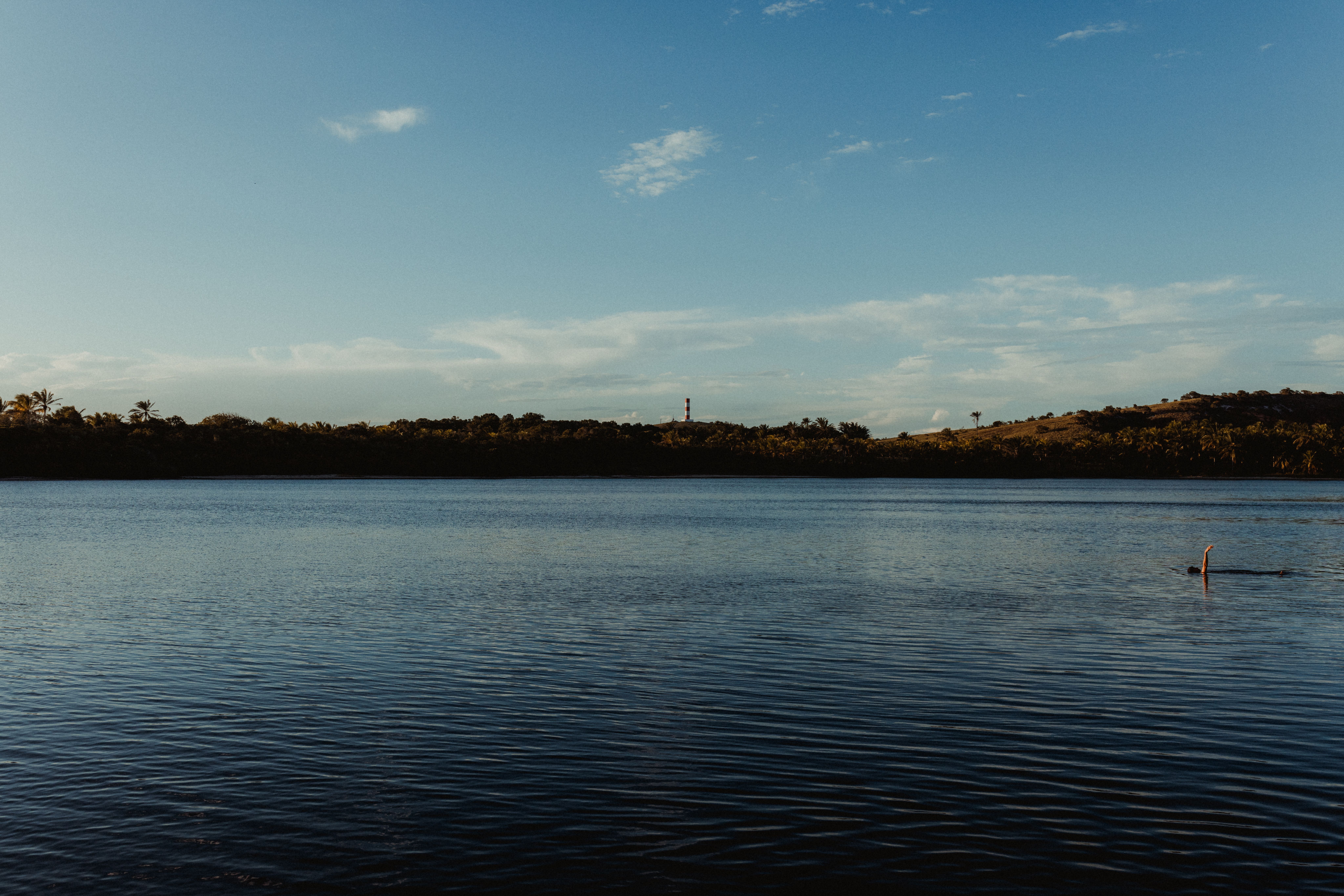 A tranquil view of Bahia's coastline at sunset with a distant lighthouse.