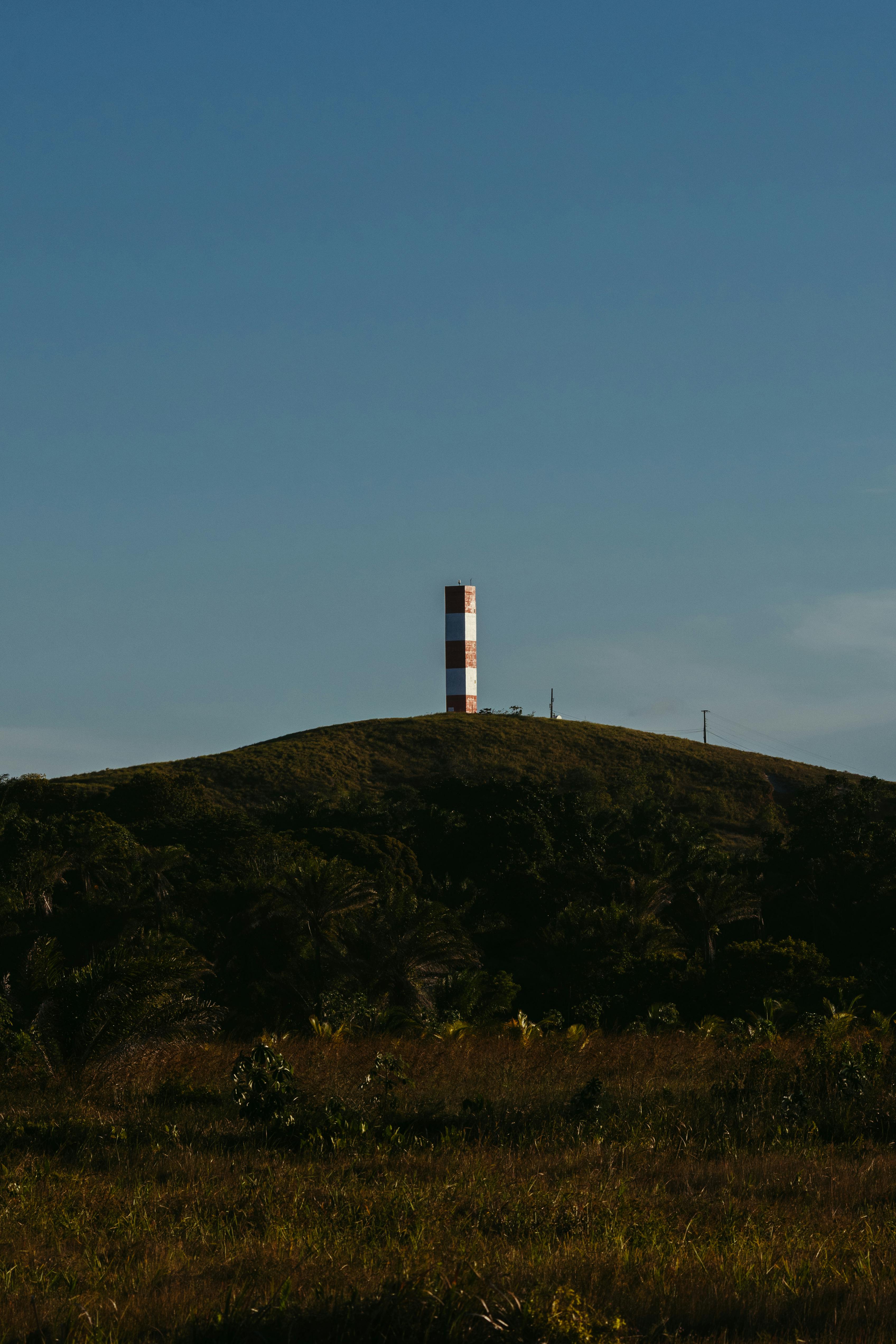 A solitary beacon stands on a hill under a clear blue sky in Marau, Bahia, Brazil, offering a serene landscape view.