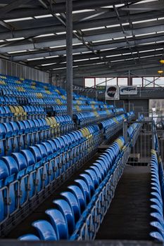 View of an empty stadium grandstand with blue and yellow seats under a metal roof.