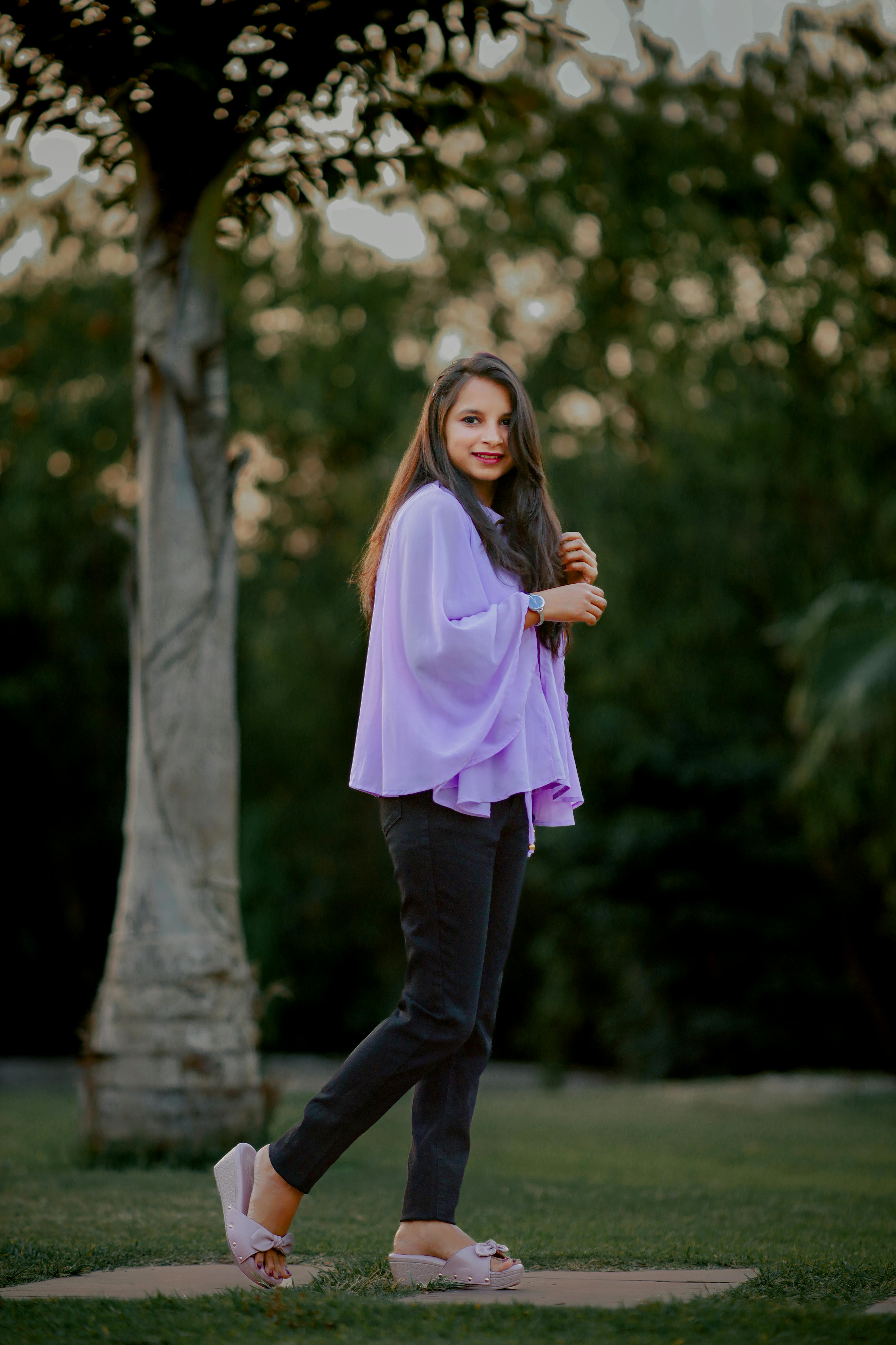Stylish woman in purple blouse posing in park during twilight, showcasing casual elegance.