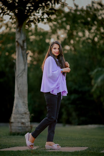 Stylish woman in purple blouse posing in park during twilight, showcasing casual elegance.