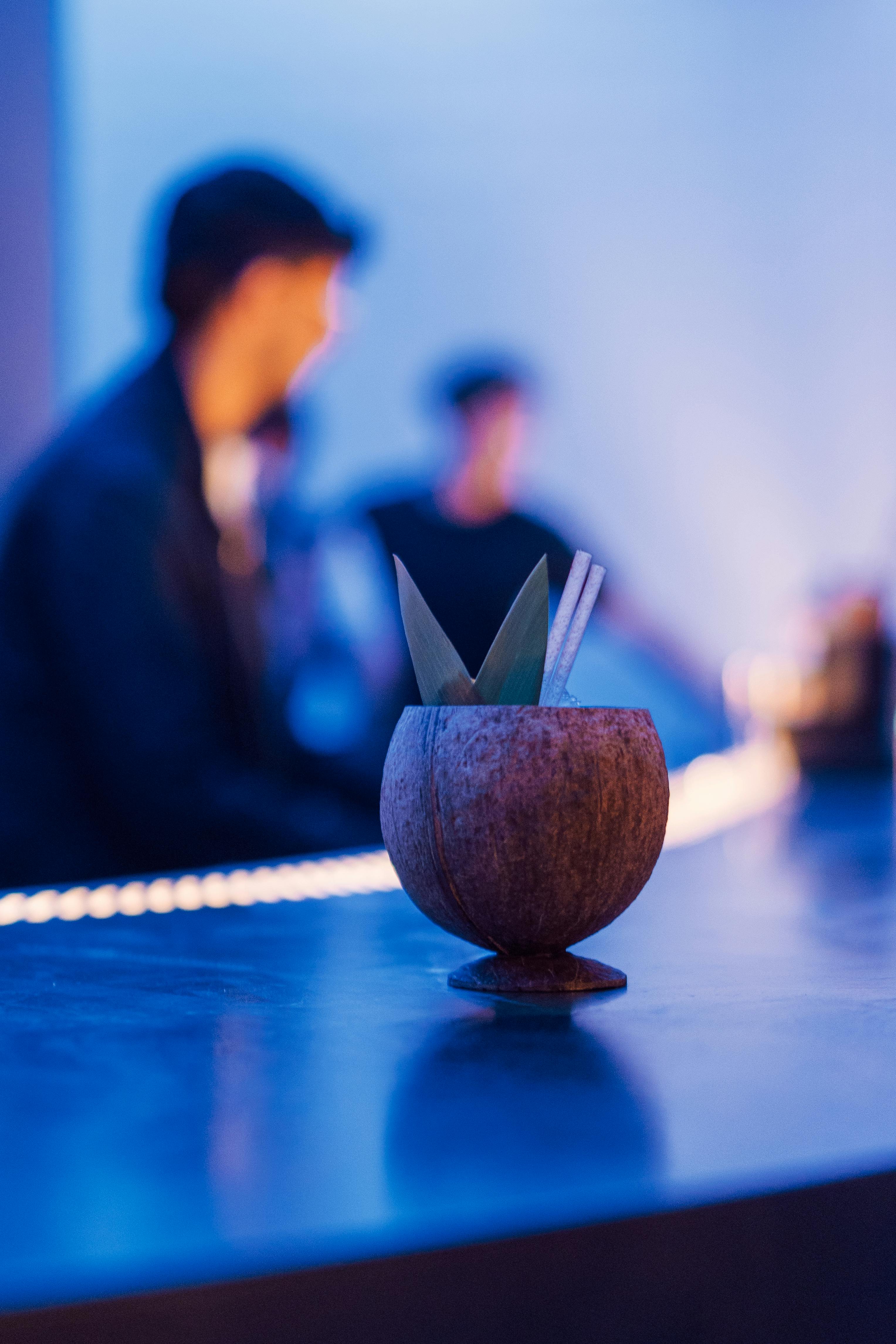 無料 バーカウンターにストロー付きのココナッツカクテル、背景にぼやけた人々。 写真素材