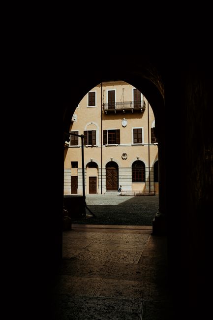 Dramatic view of an Italian courtyard framed through a dark archway, showcasing historic architecture.