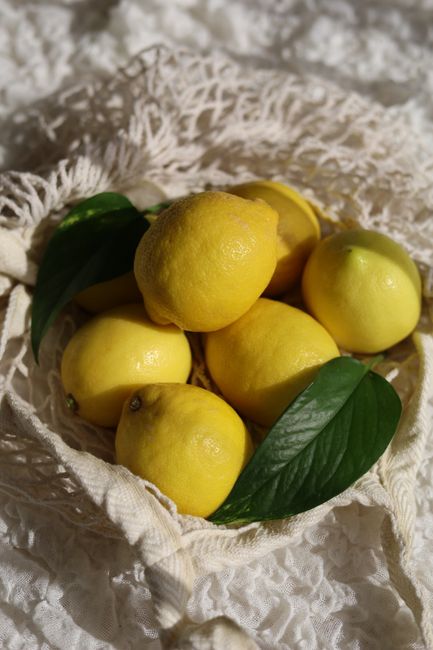 Bright yellow lemons arranged with green leaves on a textured fabric in sunlight.