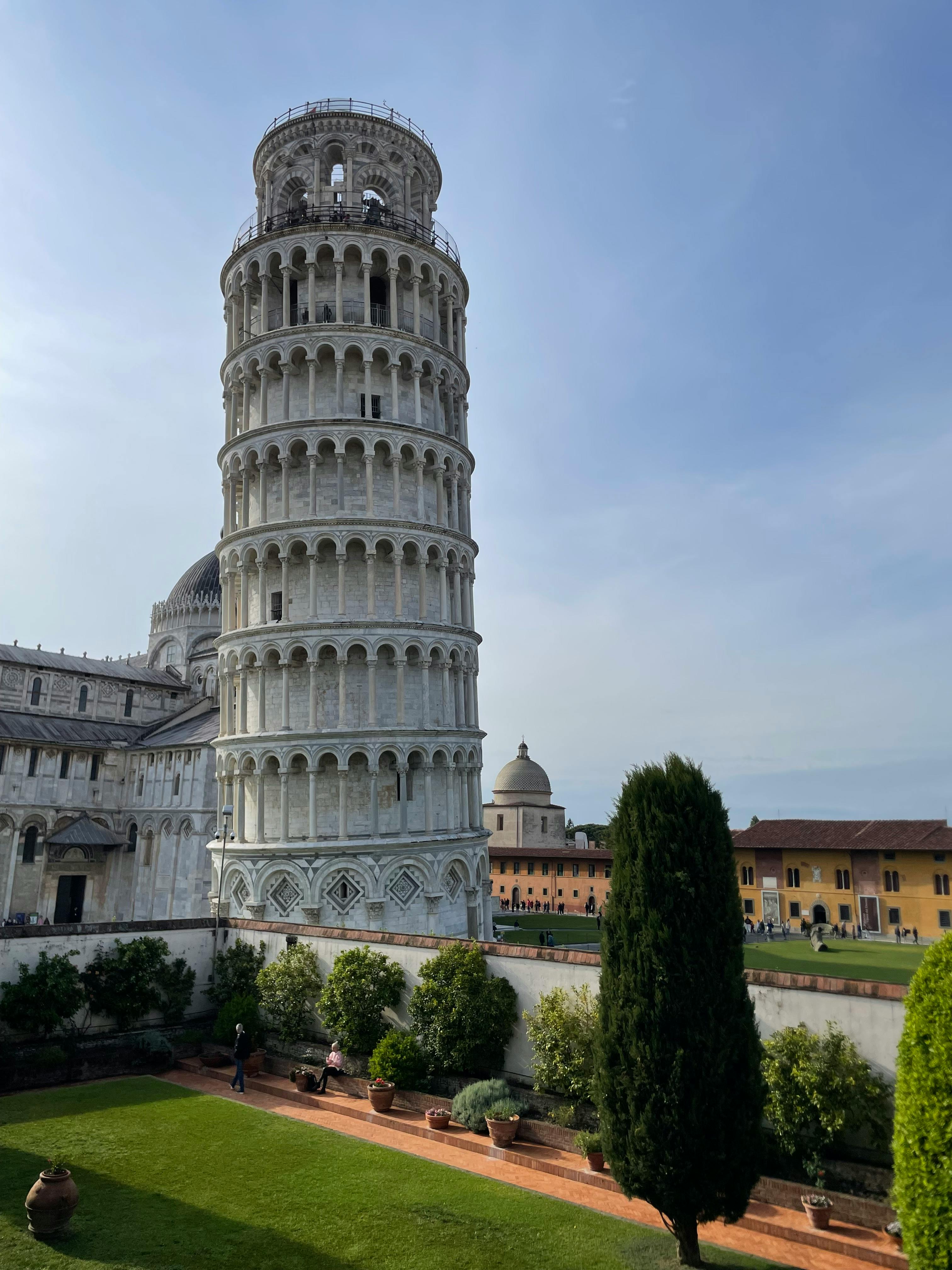 Gratis Det skjeve tårnet i Pisa badet i sollys, fotografert fra en livlig hageutsikt i Italia. Arkivbilde