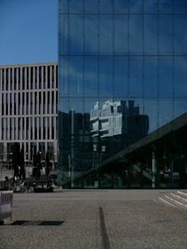 Glass building reflecting another architectural structure downtown on a sunny day.