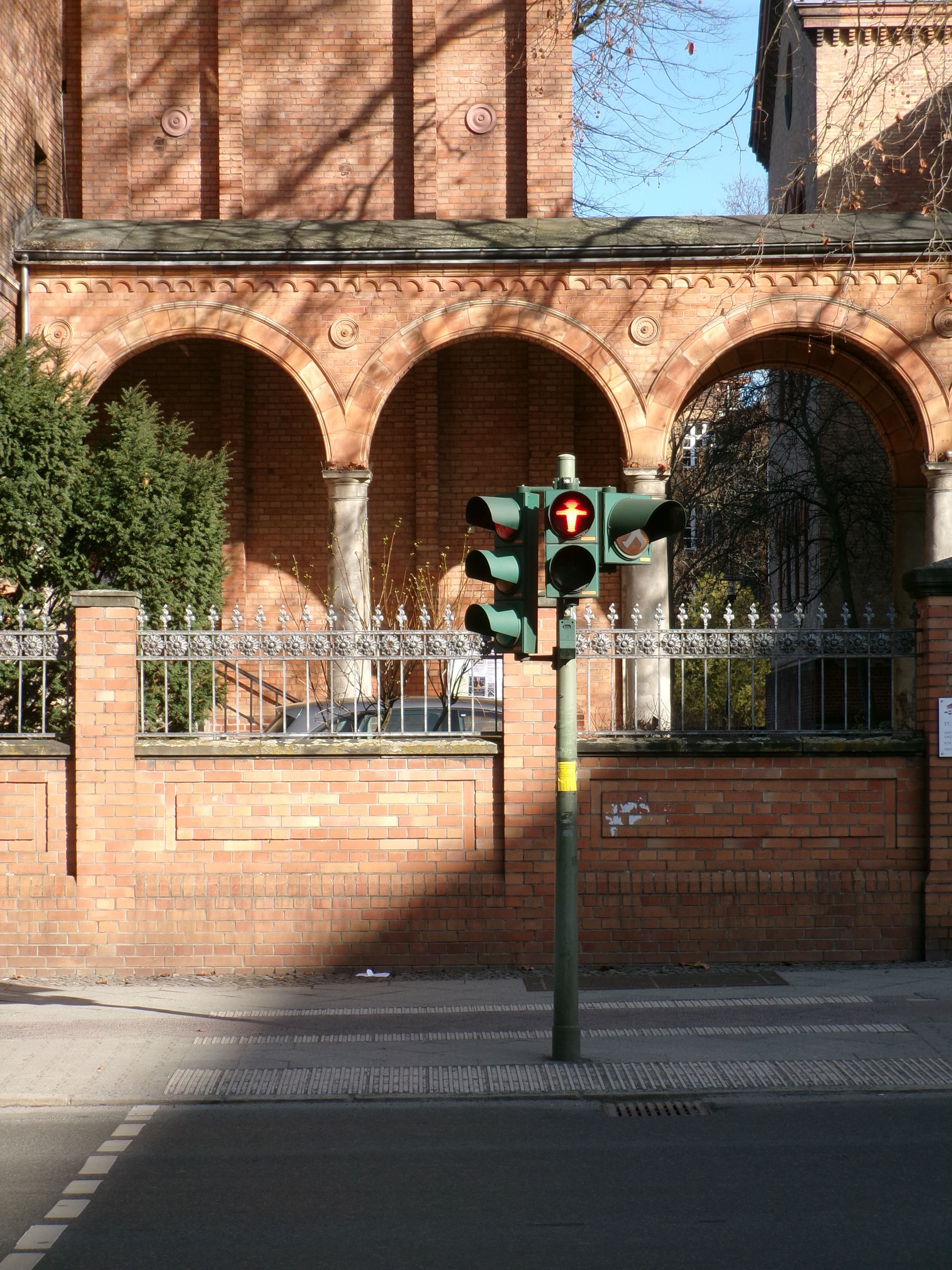 A traffic light stands before an arched brick building facade under bright sunlight.