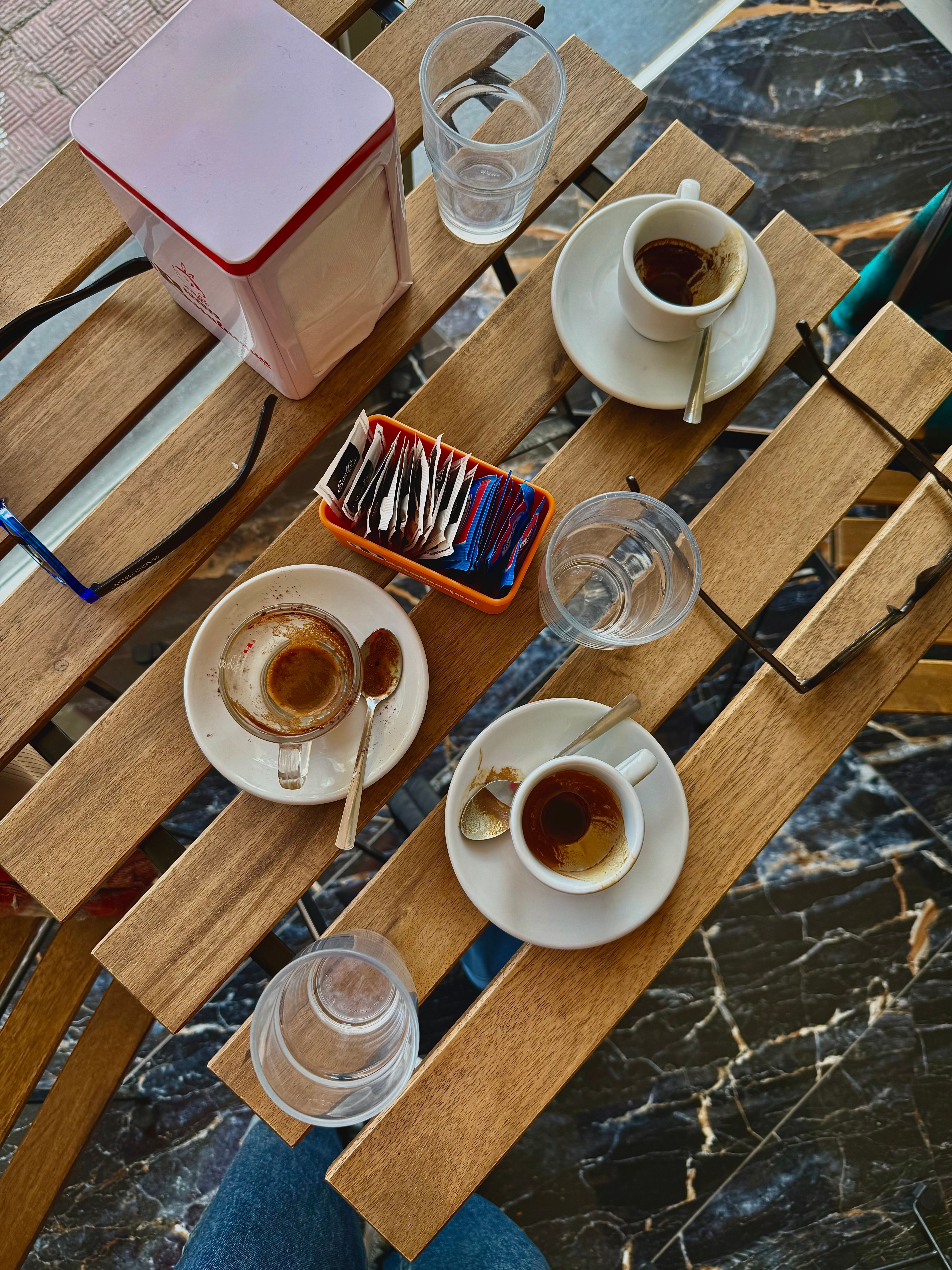Top-down view of espresso cups, glasses, and sugar packets on a wooden table in a café.