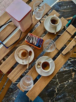 Top-down view of espresso cups, glasses, and sugar packets on a wooden table in a café.
