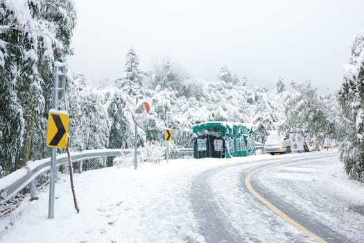Scenic snowy mountain road with traffic signs and a tent under heavy snow. Ideal winter travel setting.