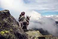 Siberian Husky Beside Woman Sitting on Gray Rock Mountain Hill While Watching Aerial View