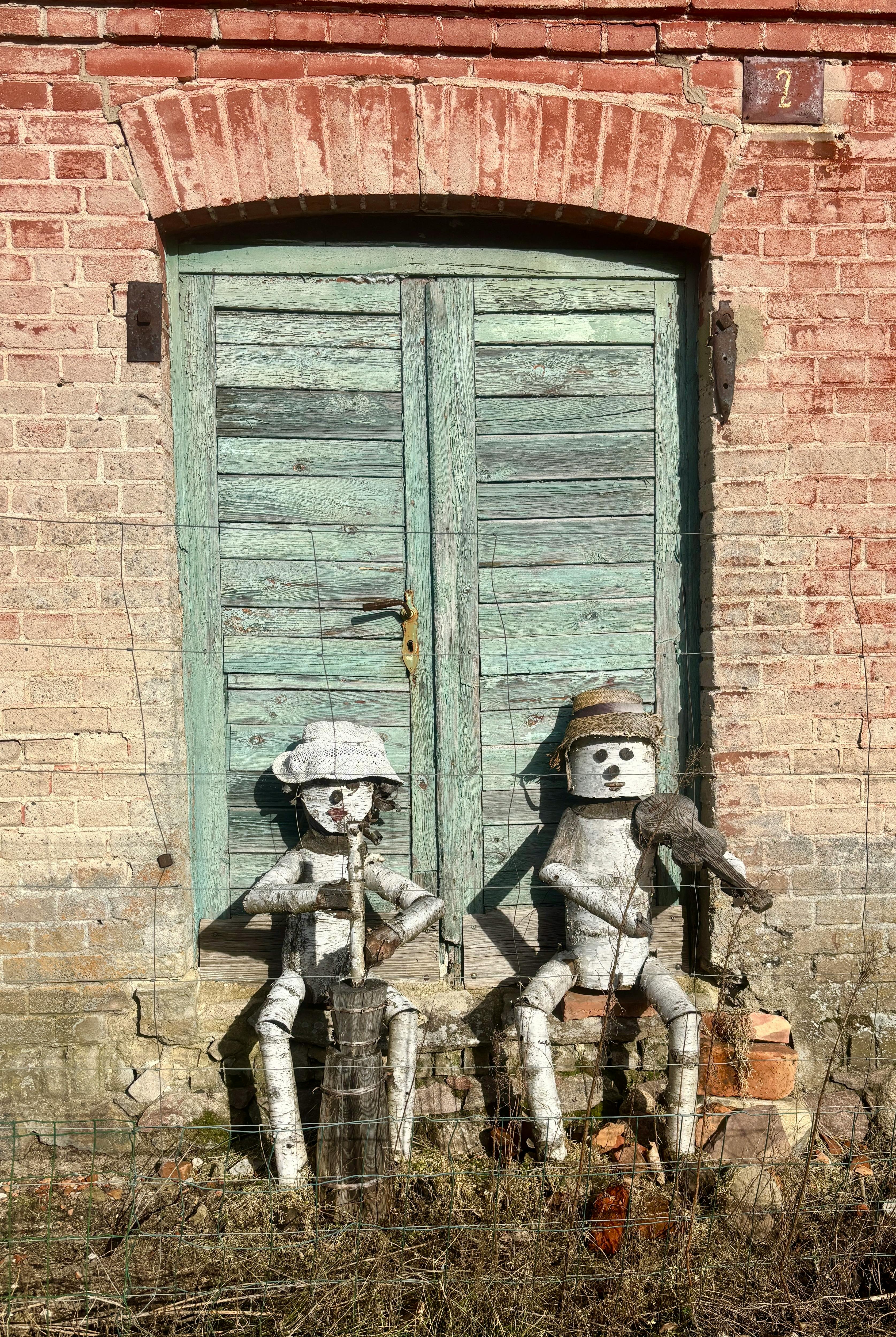 Gratis To metalrobotskulpturer sidder ved en rustik dør på en solskinsdag. Lagerfoto