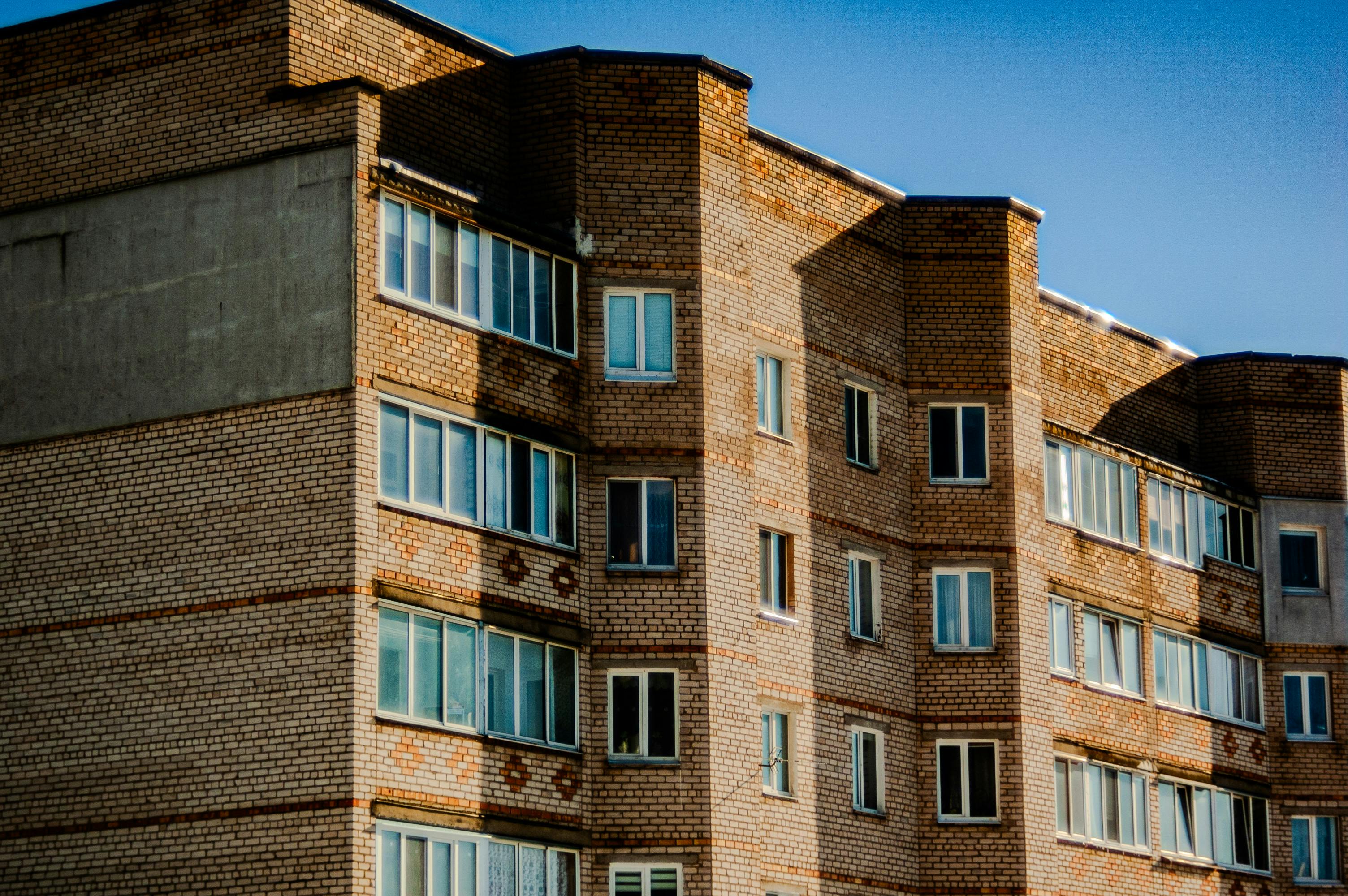 無料 澄み切った青空の下にある、複数の窓があるレンガ造りのアパートの正面のクローズアップ写真。 写真素材