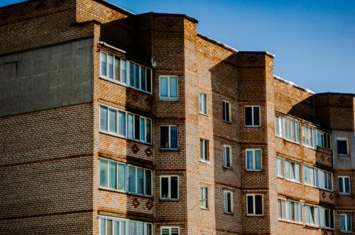 Free Close-up view of a brick apartment building facade with multiple windows under a clear blue sky. Stock Photo