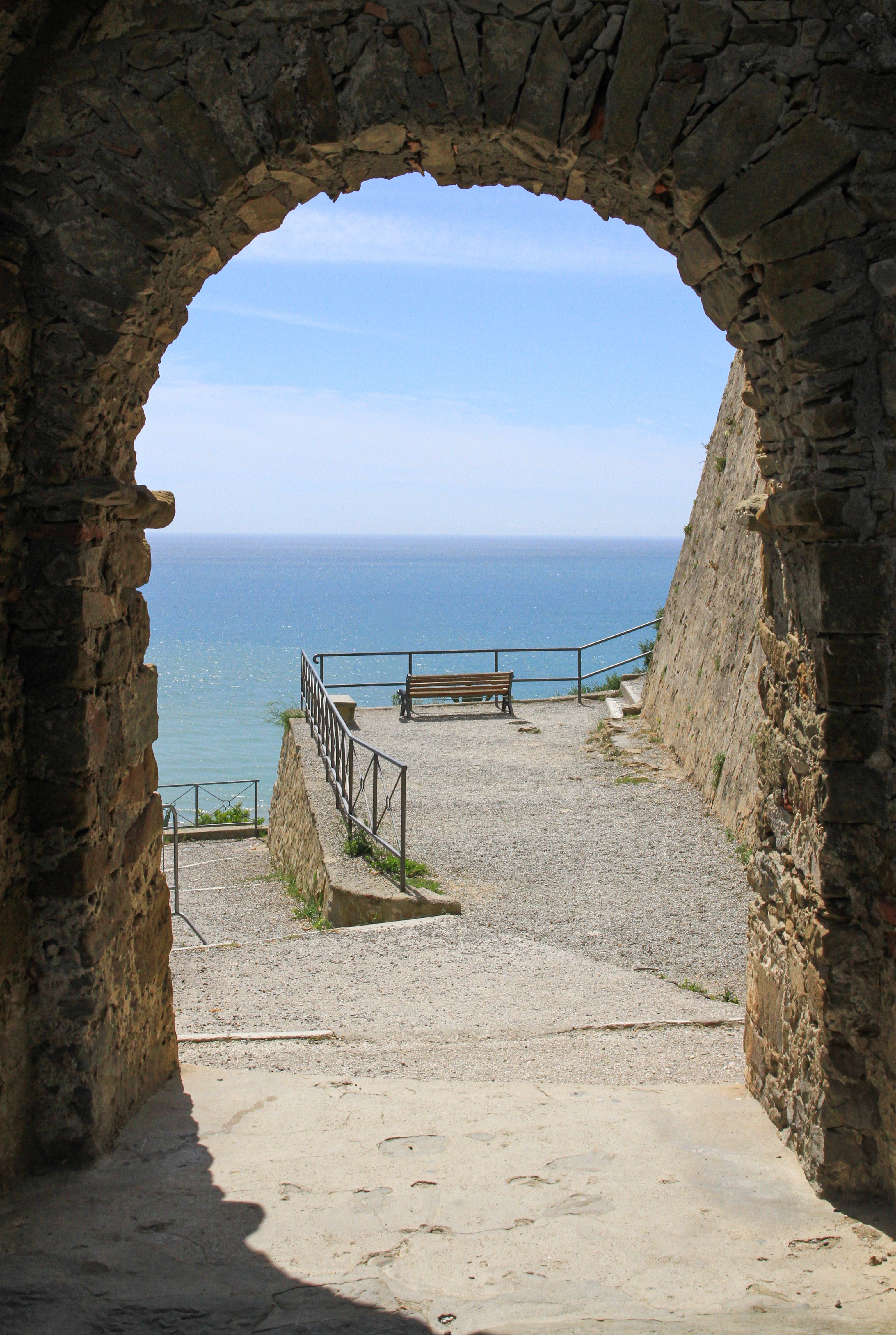 Free View through a historic stone archway leading to a peaceful seaside vista. Stock Photo