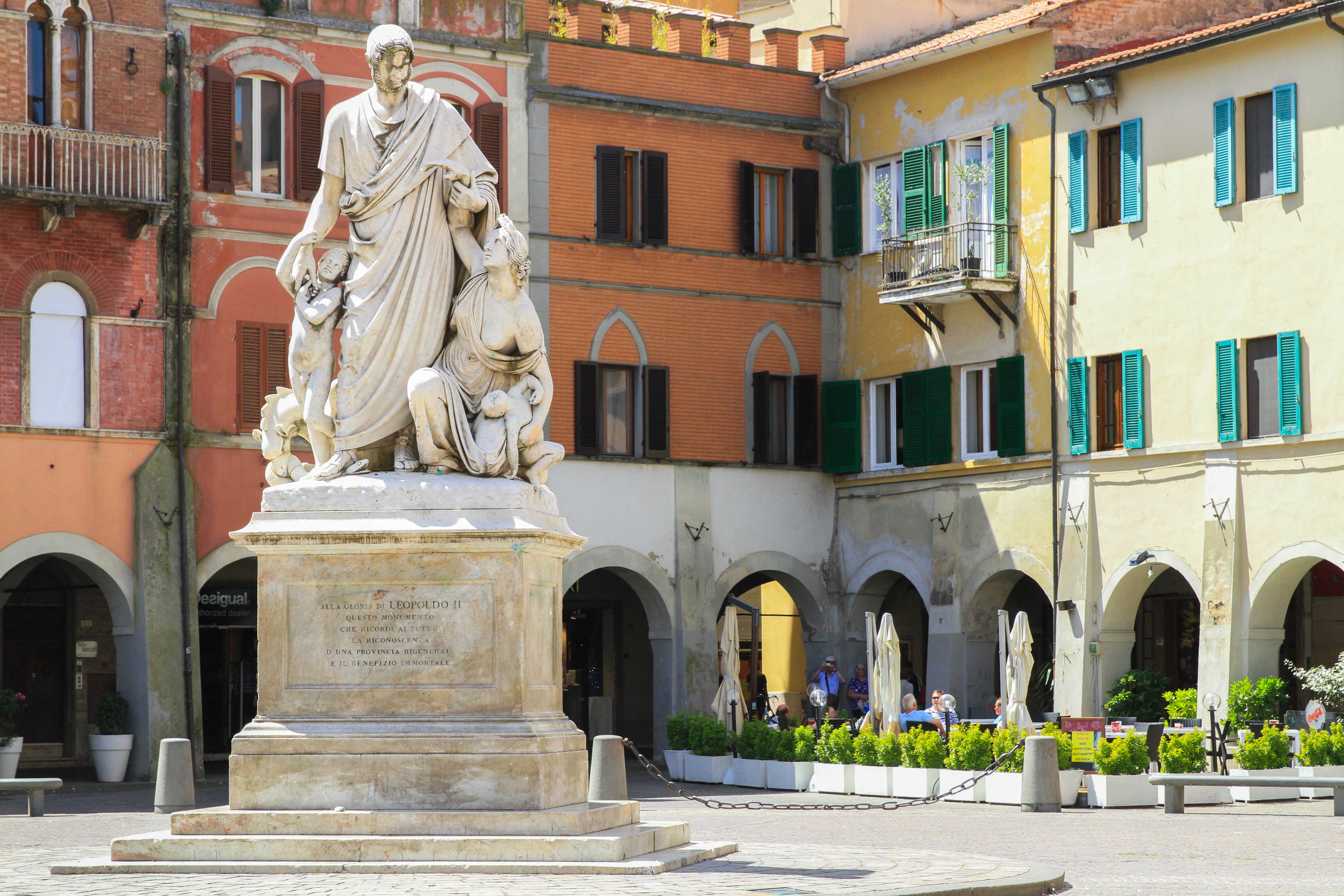 Free A marble statue in a vibrant Italian square with historic colorful buildings. Stock Photo