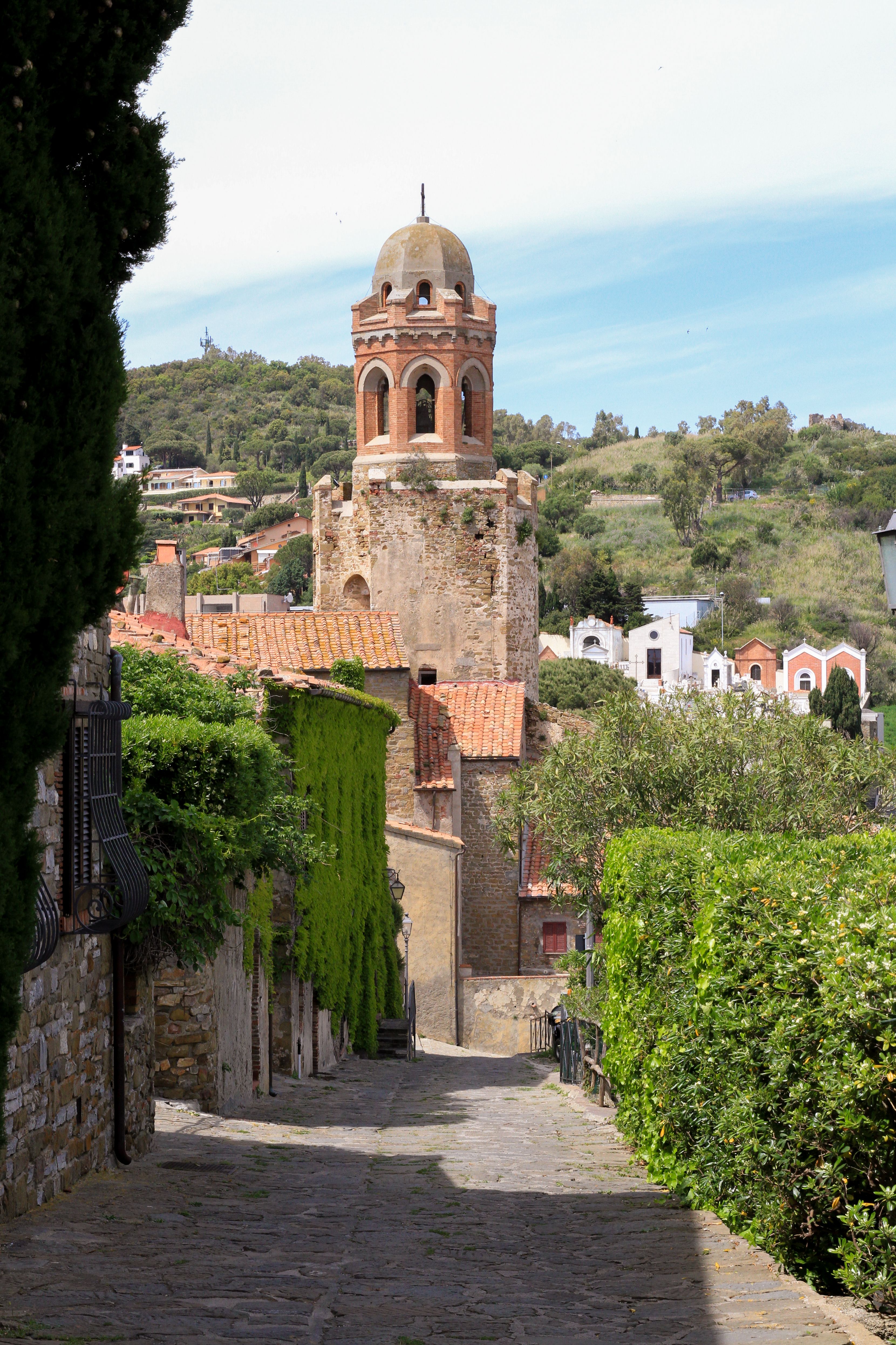 Free Beautiful view of a historic bell tower surrounded by lush greenery in a quaint village setting. Stock Photo