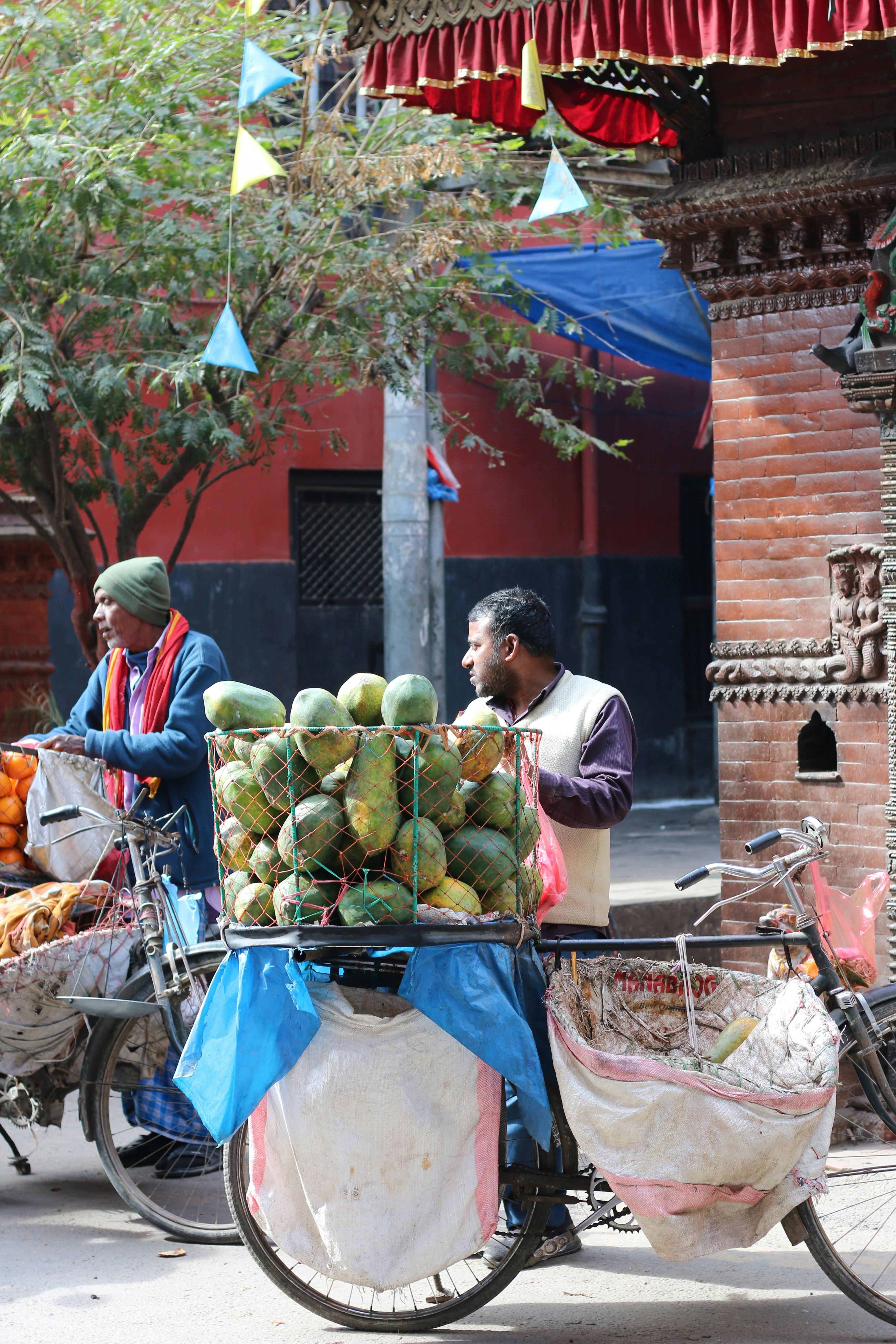 無料 カトマンズの活気ある市場で自転車に乗った色鮮やかな果物売りたち。 写真素材