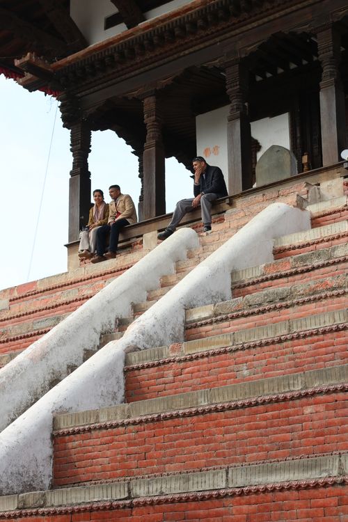 Free Three adults seated on historic temple steps in Kathmandu, Nepal. Stock Photo