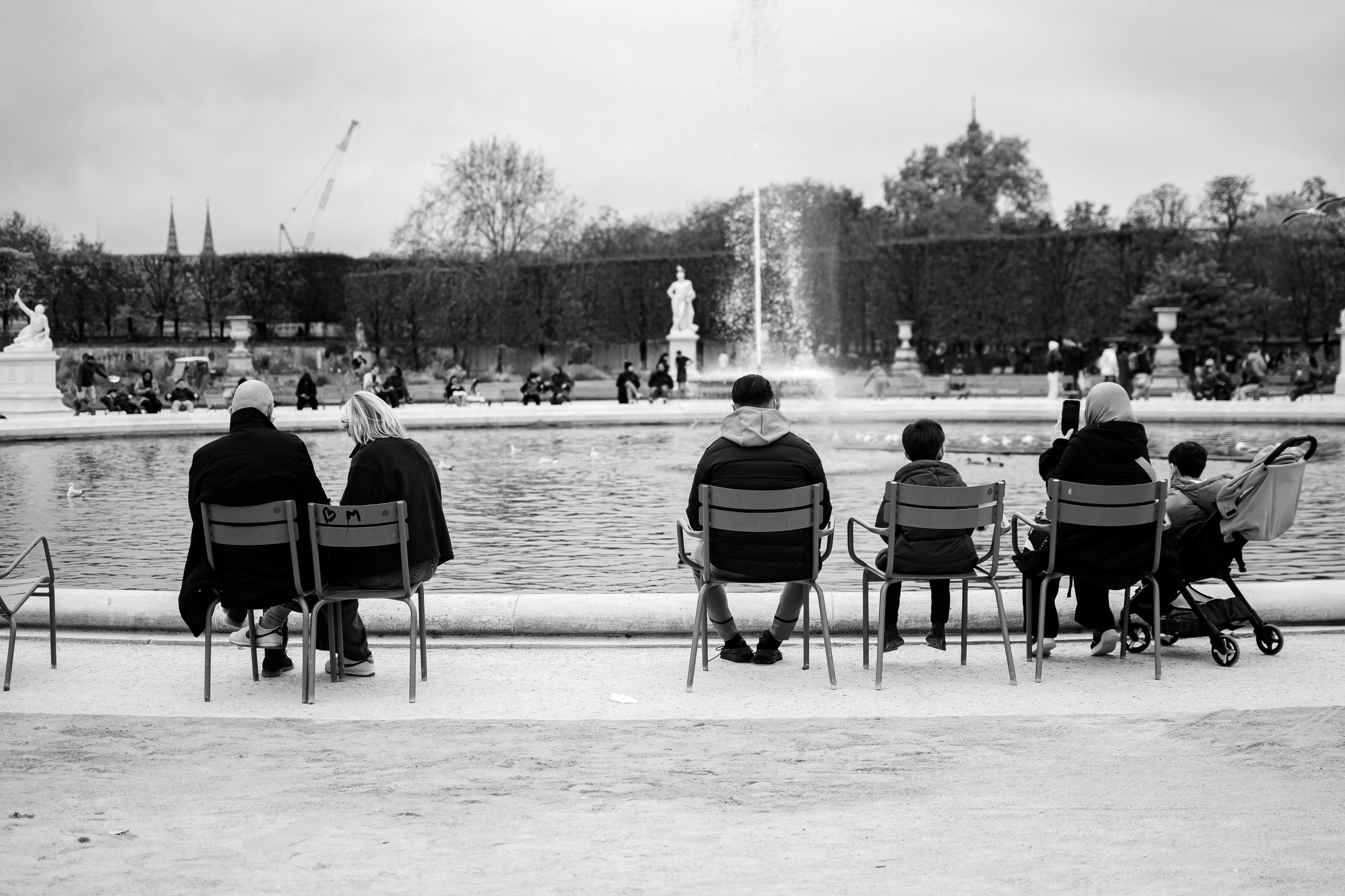 無料 パリの公園の噴水のそばでくつろぎながら、穏やかな一日を楽しむ人々。 写真素材