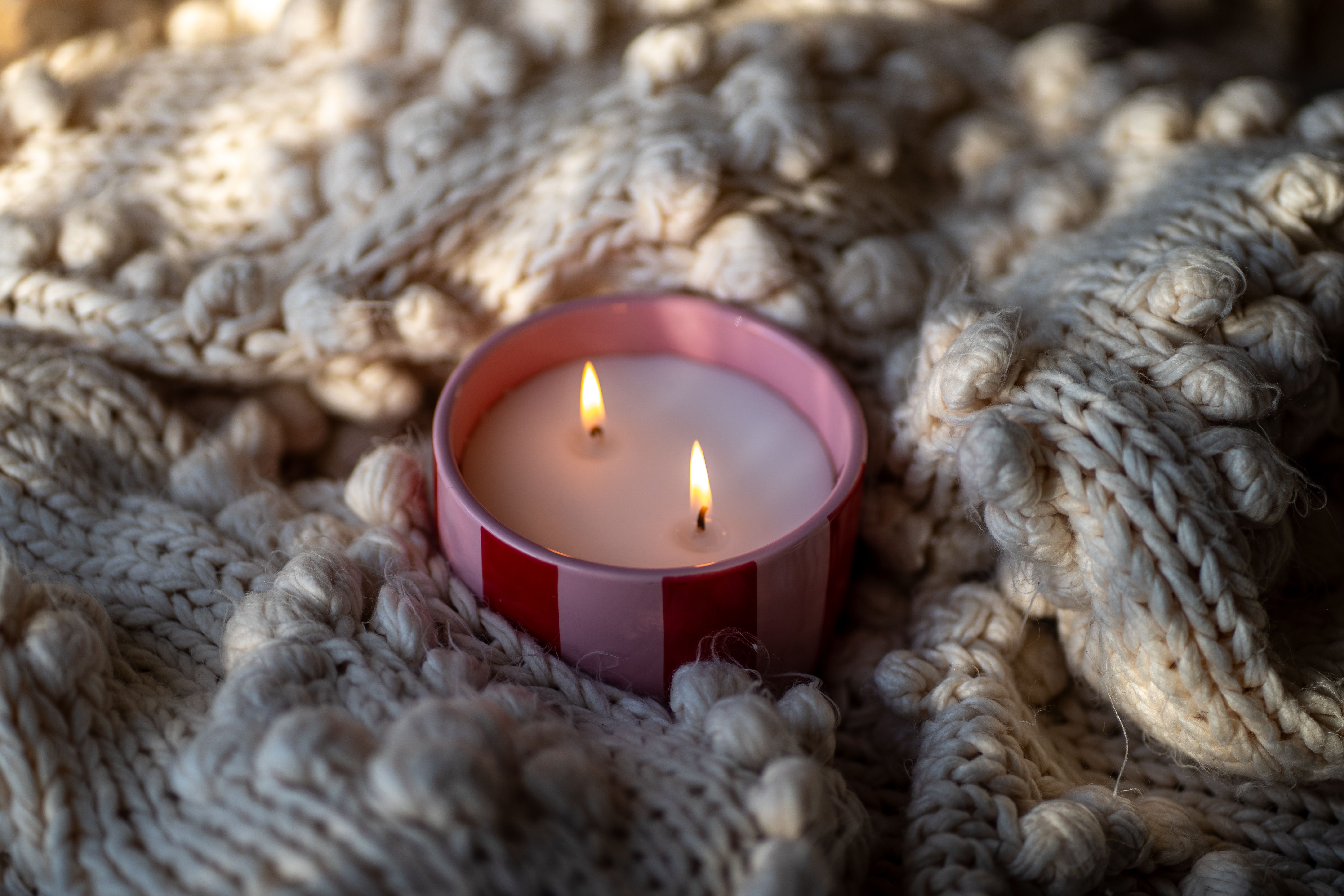 Warm candlelight nestled on a chunky knit blanket evokes a cozy atmosphere.