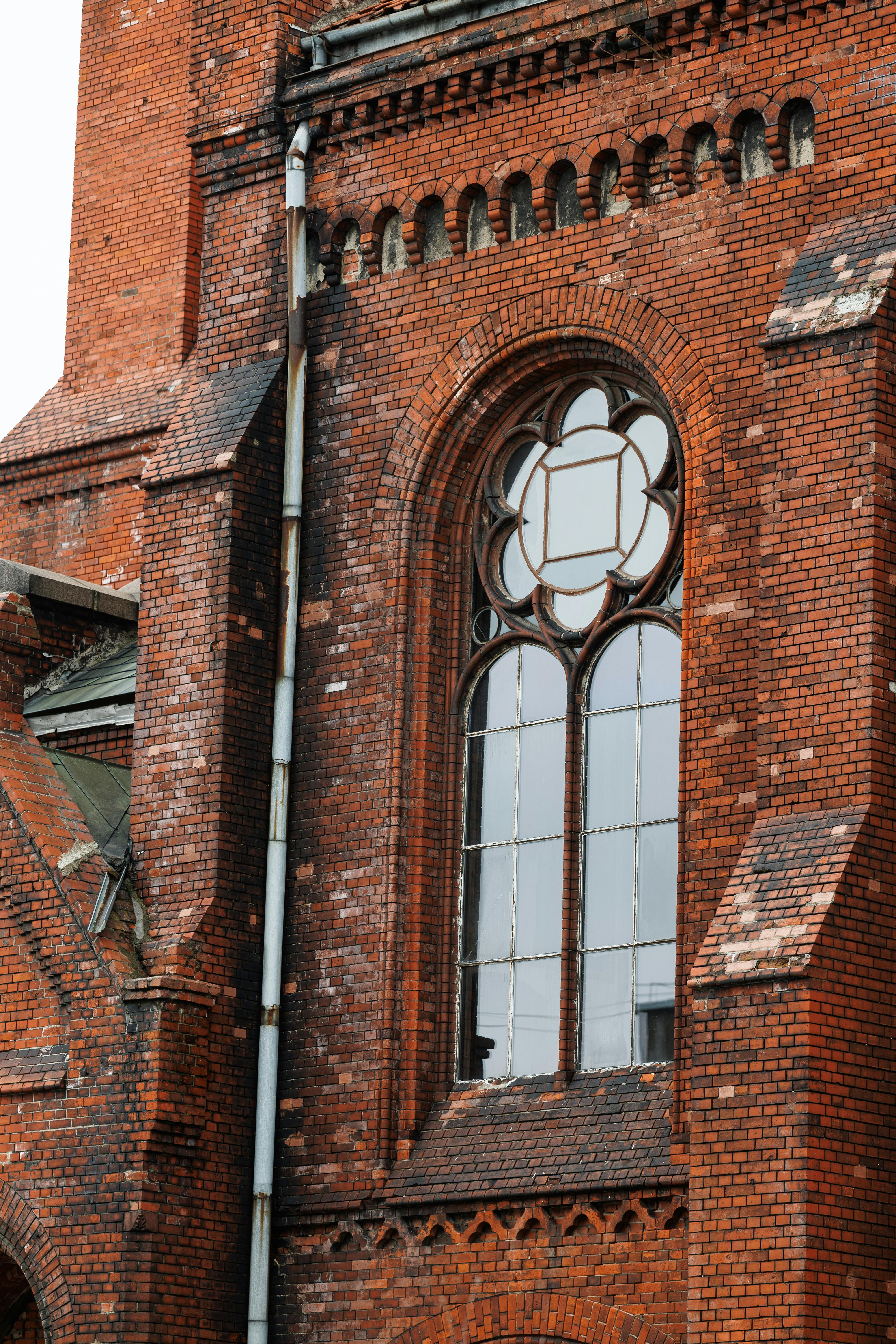 бесплатная Детальный вид фасада готической церкви из красного кирпича в Черняховске, демонстрирующий богато украшенные витражи. Стоковое фото