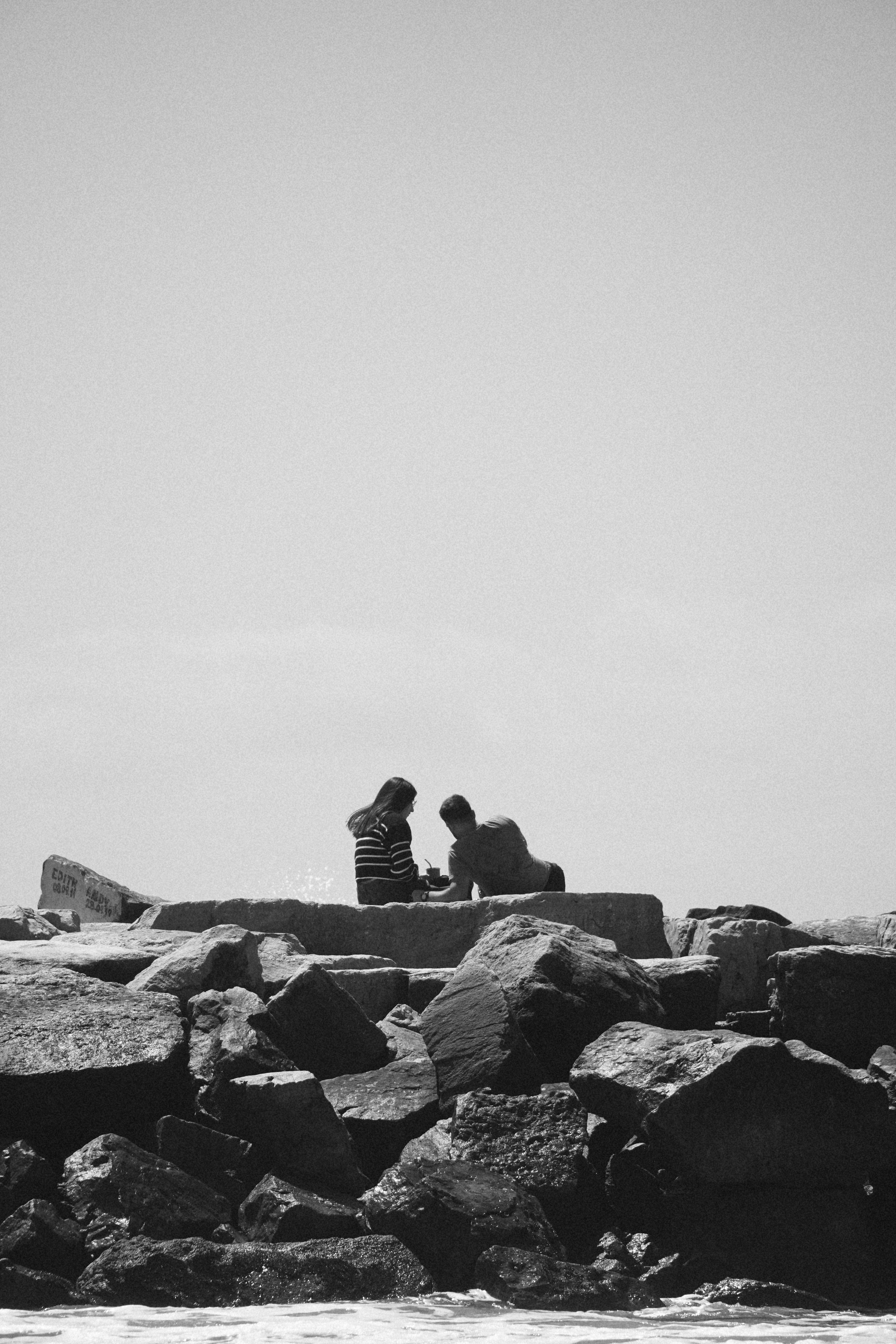 Free Silhouette of two people seated on coastal rocks against a clear sky. Stock Photo