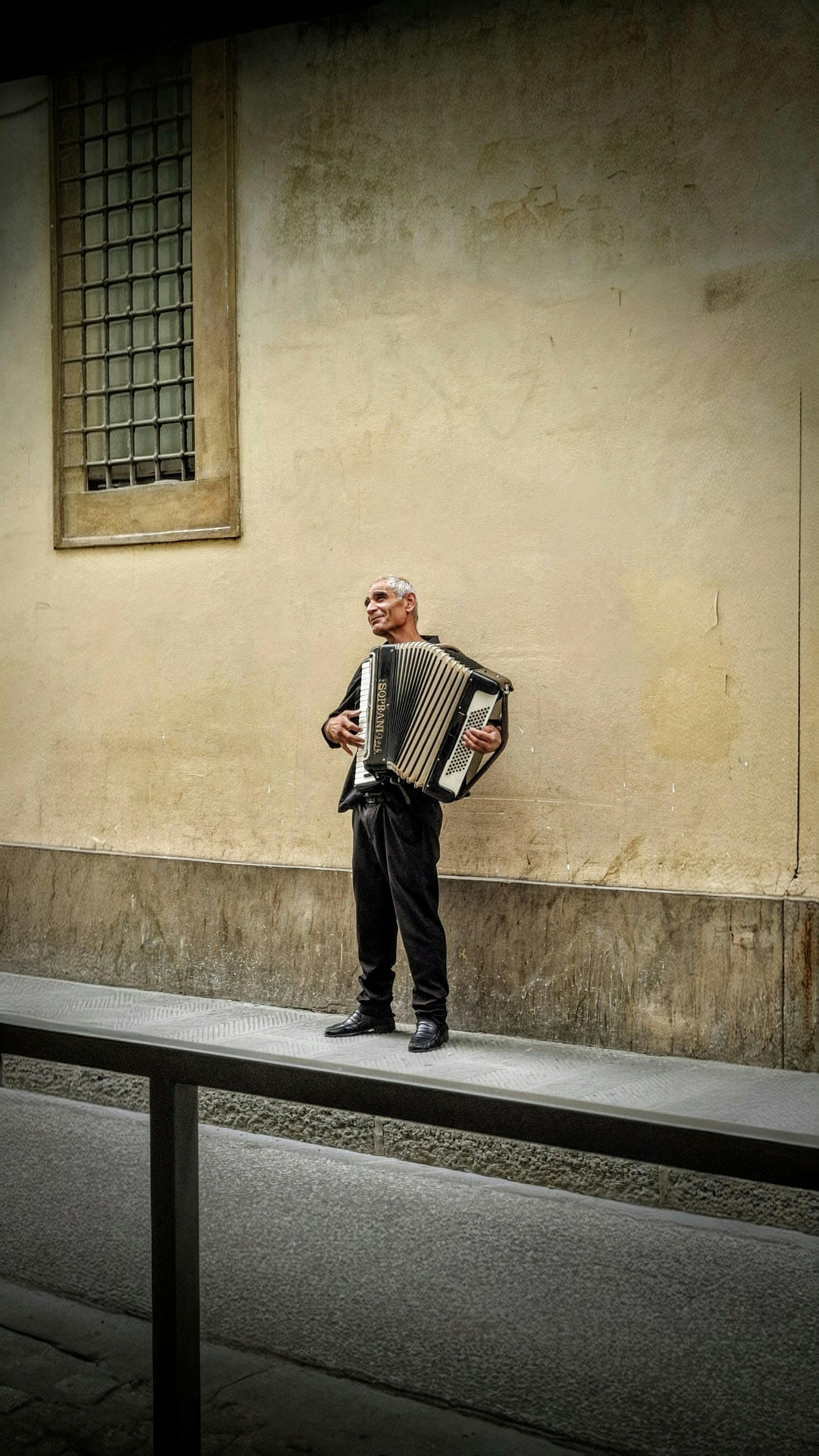 Gratis En gatemusikant spiller trekkspill mot en gammel bymur. Arkivbilde