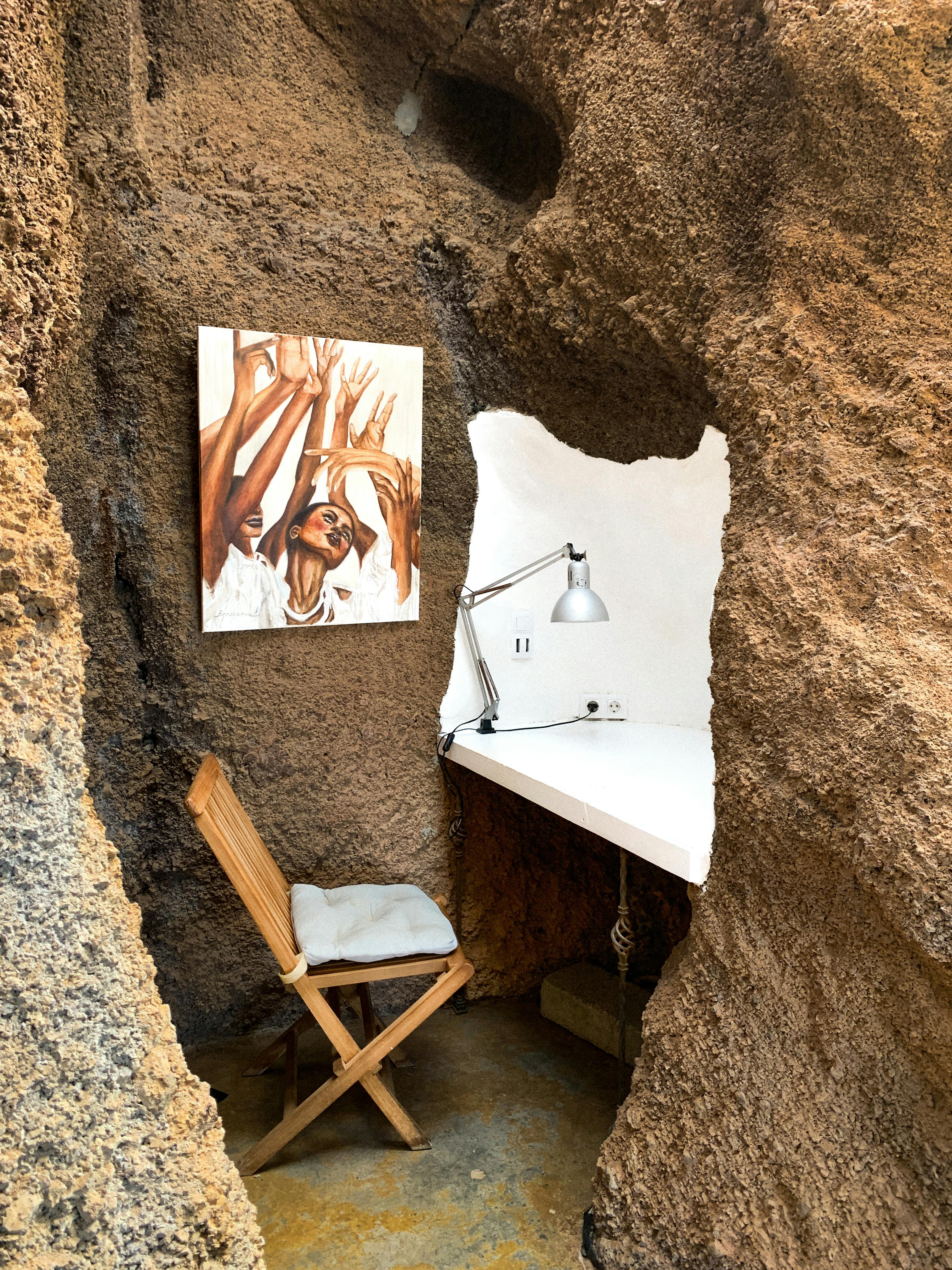 бесплатная Творческое рабочее пространство в скальной пещере с современным столом и выразительными произведениями искусства. Стоковое фото