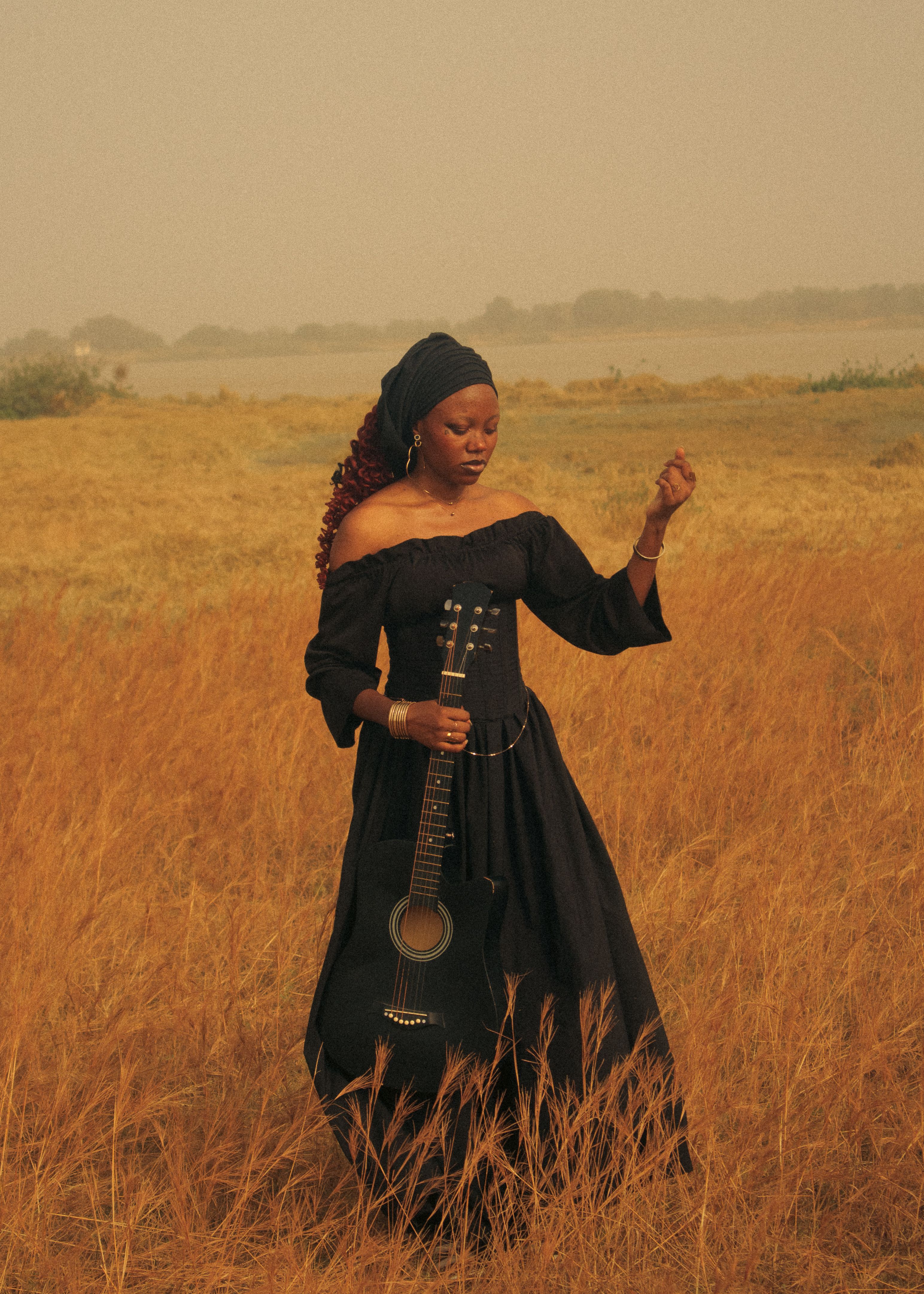 A serene portrait of a woman in a black dress holding an acoustic guitar in a golden field.