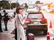 在泰国一条繁忙的街道旁，两名妇女带着行李，在一辆停着的汽车边等待