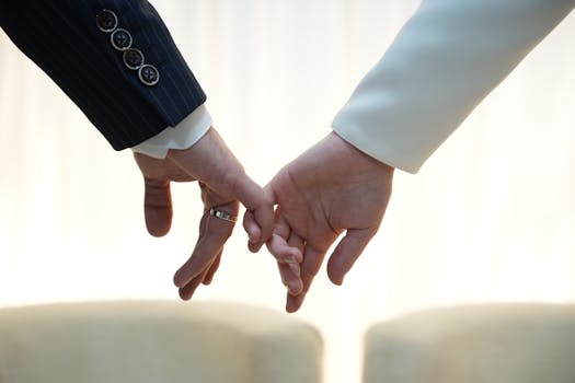 A close-up of two adults tenderly holding hands in formal suits, symbolizing unity and connection.