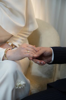 Close-up of a couple holding hands, showcasing wedding rings and attire, symbolizing love and commitment.