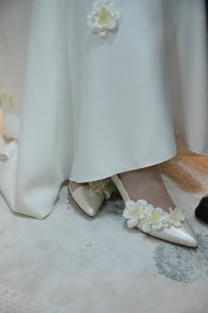 Close-up of bridal shoes adorned with delicate floral designs under a white wedding dress.