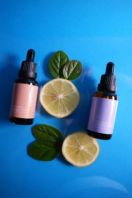 Free Flat lay of skincare dropper bottles with lemon slices on vibrant blue background. Stock Photo