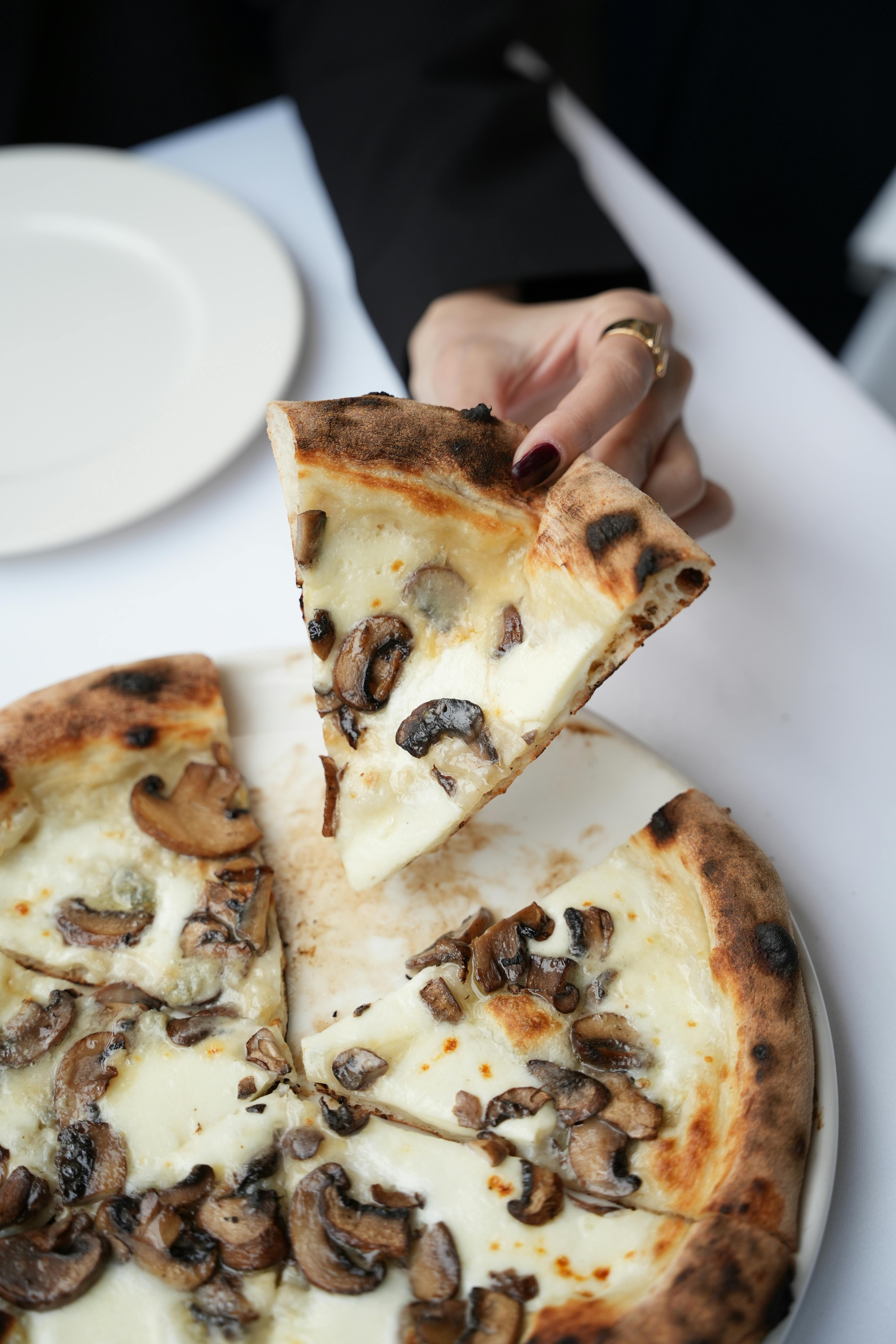 Close-up of a hand taking a slice of mushroom pizza with a creamy cheese topping.