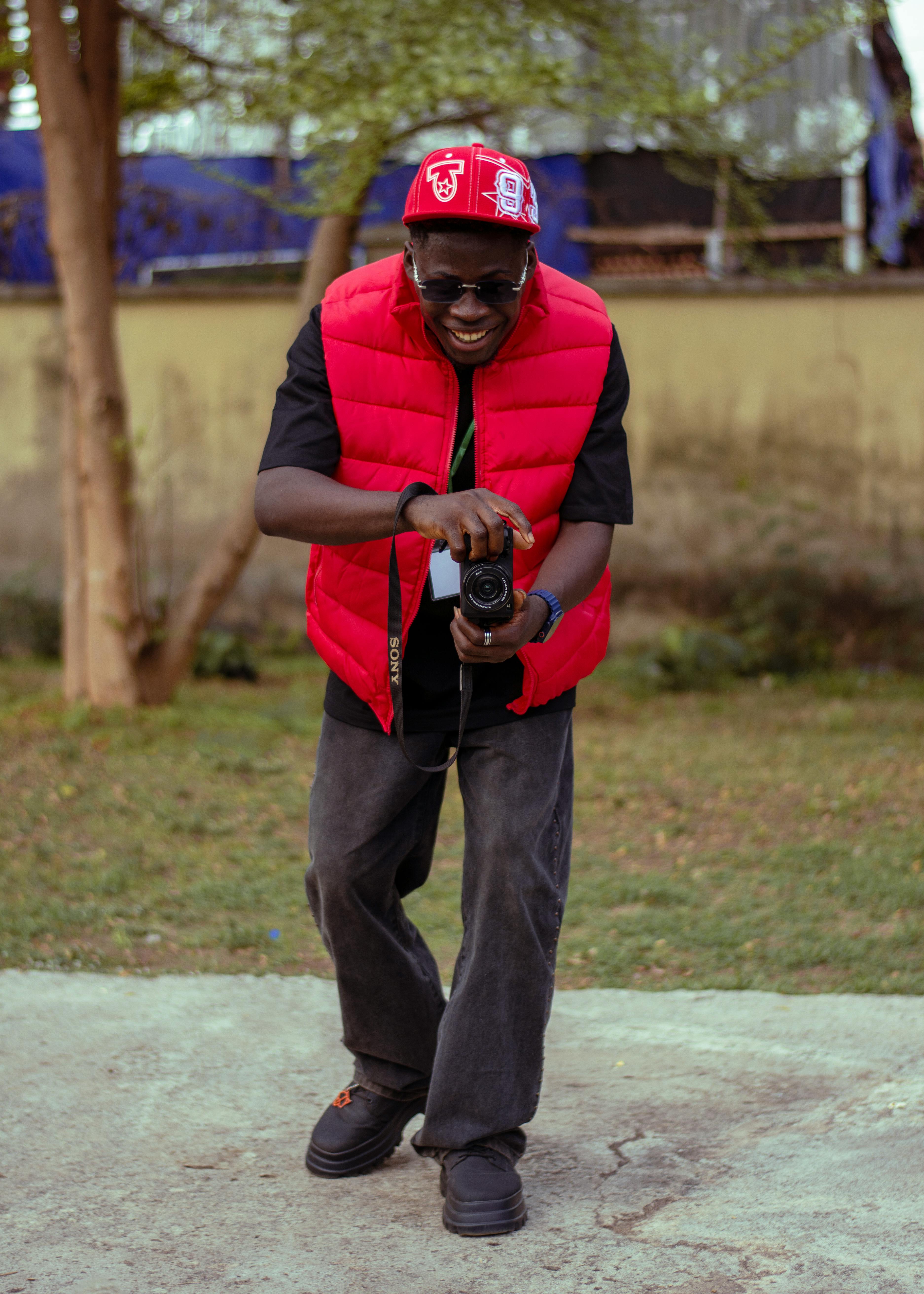 Happy photographer in casual attire holding a camera outdoors, showing a vibrant smile and personality.
