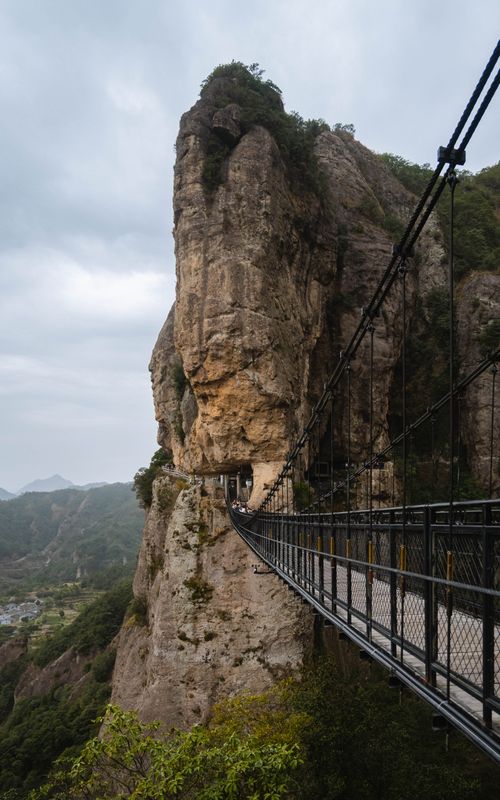 Free A dramatic suspension bridge leads to a rocky mountain tunnel on a cloudy day. Stock Photo