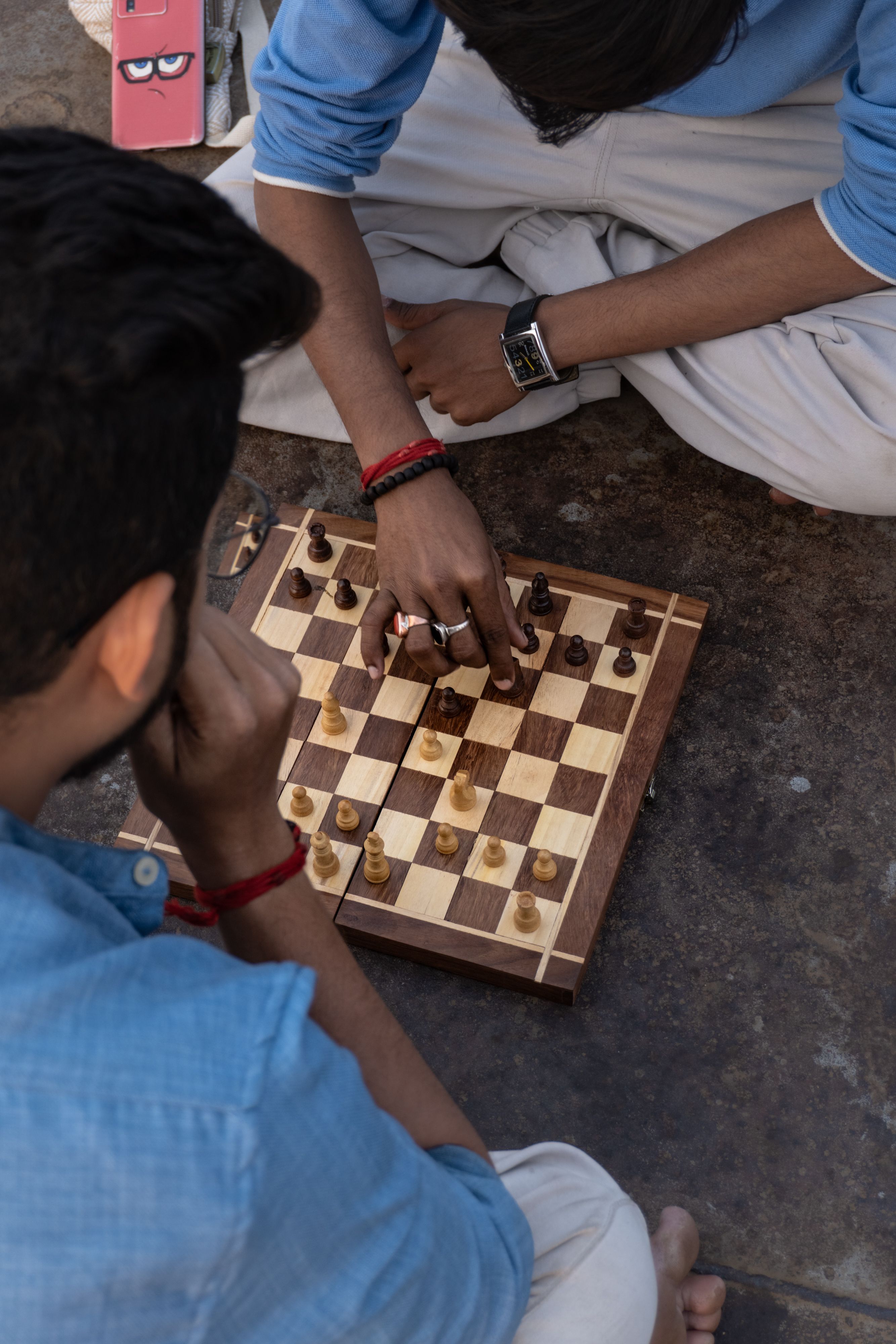 Top view of young adults intensely playing a game of chess on a wooden board outdoors.