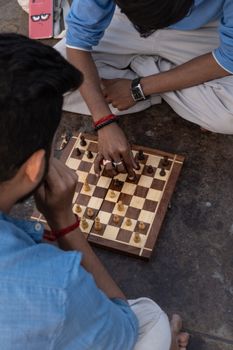 Top view of young adults intensely playing a game of chess on a wooden board outdoors.