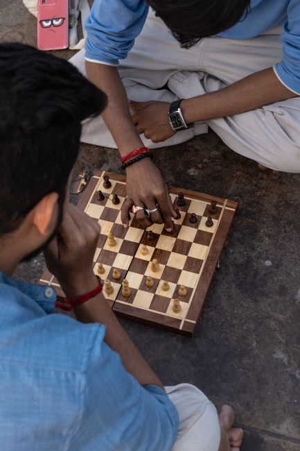 Top view of young adults intensely playing a game of chess on a wooden board outdoors.