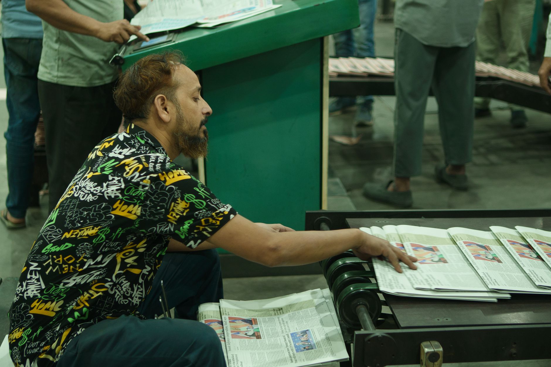 Man sorting newspapers on a conveyor belt in a busy printing press environment.