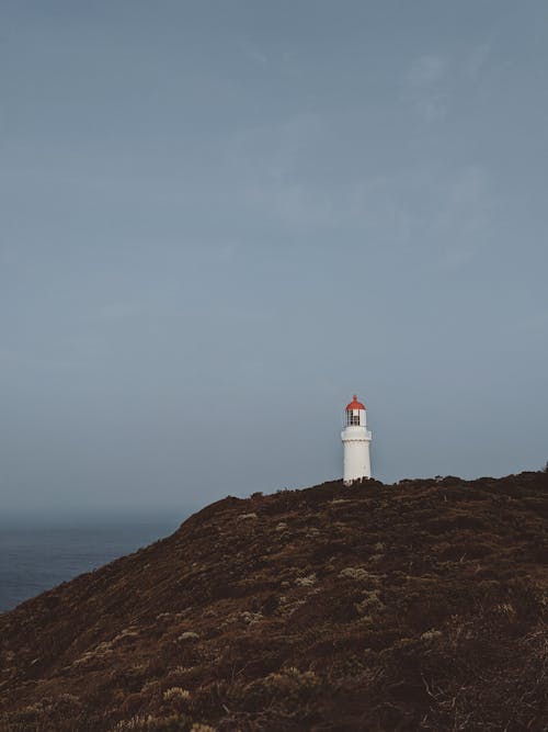 White Lighthouse on Brown Hill Under White Clouds