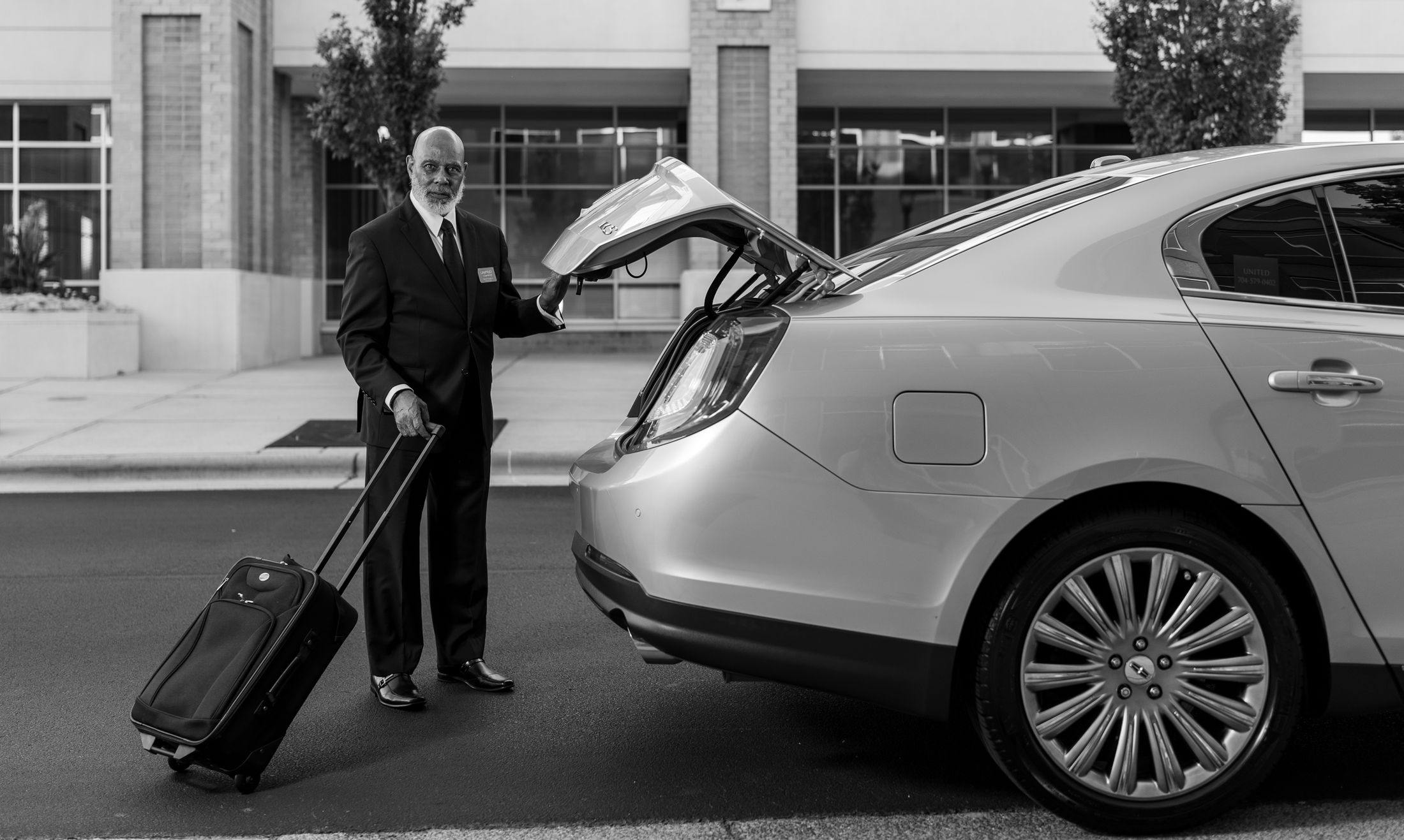 A chauffeur in a suit loading luggage into a clean luxury car.