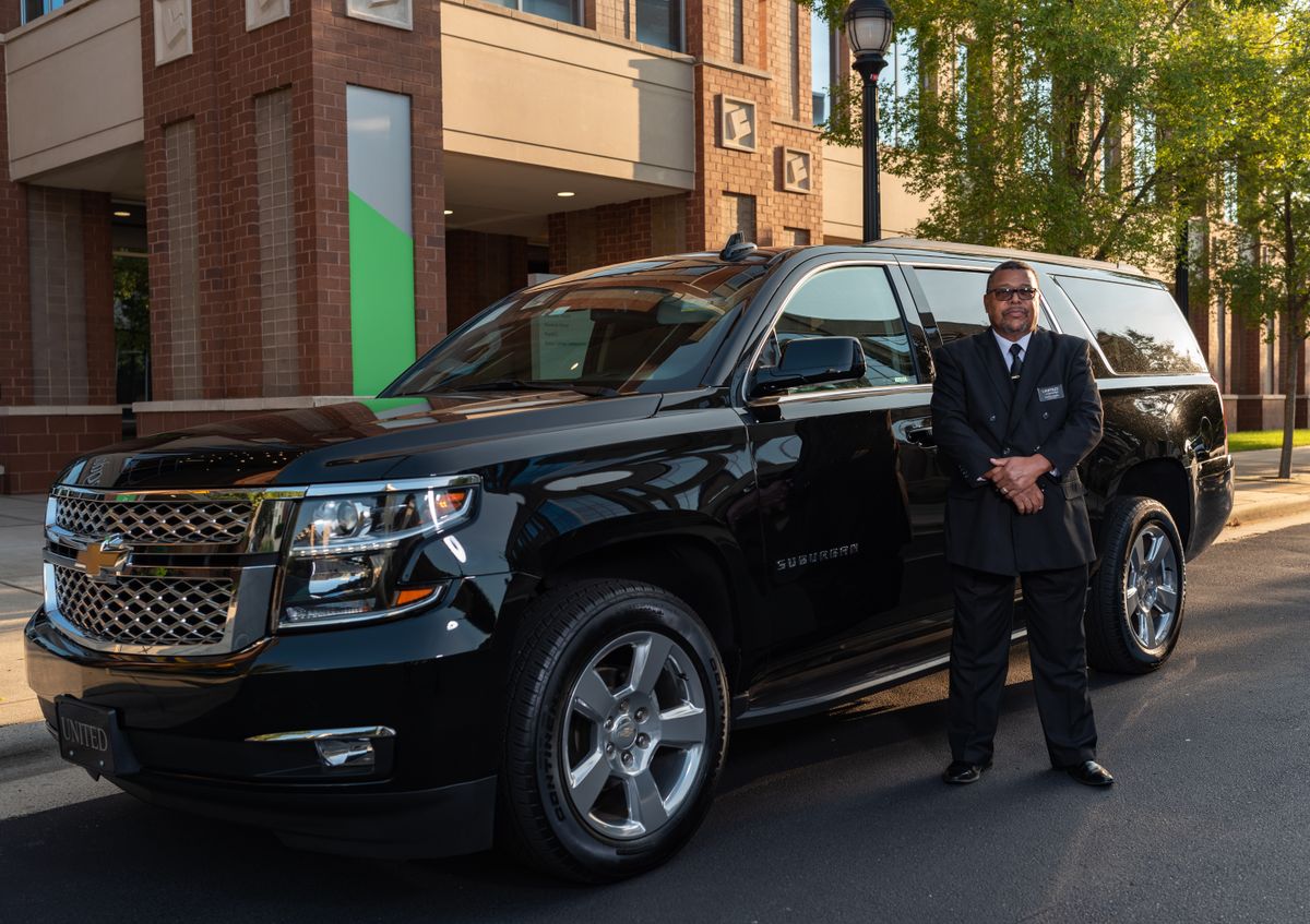 Chauffeur beside a black luxury SUV outside a modern building